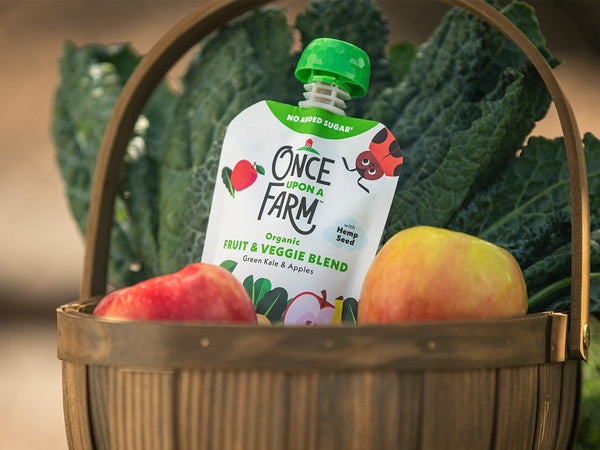 Once Upon a Farm Green Kale & Apples pouch in a basket with fresh apples and kale