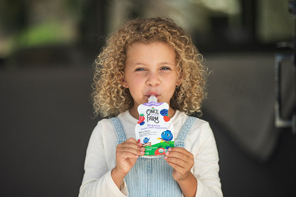 close-up shot of a young girl eating a once upon a farm smoothie pouch