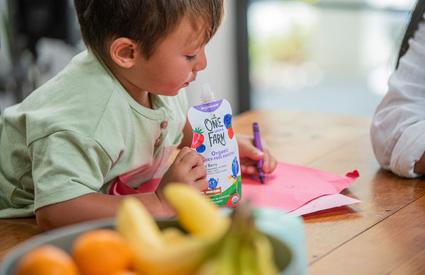 young boy coloring with a crayon, while eating a Once Upon a Farm Dairy-Free Smoothie pouch
