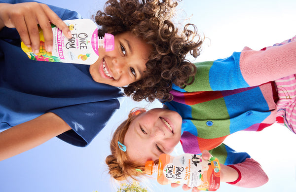 two kids holding Once Upon a Farm pouches, looking down at the camera and smiling
