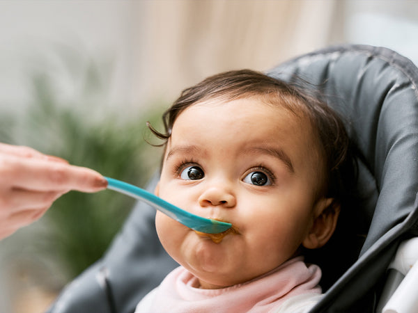 baby being fed baby food off of a spoon, while sitting in a high chair