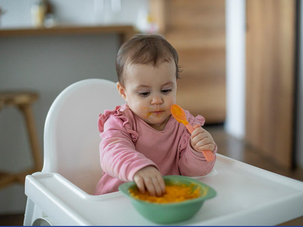 baby in high chair eating baby food puree