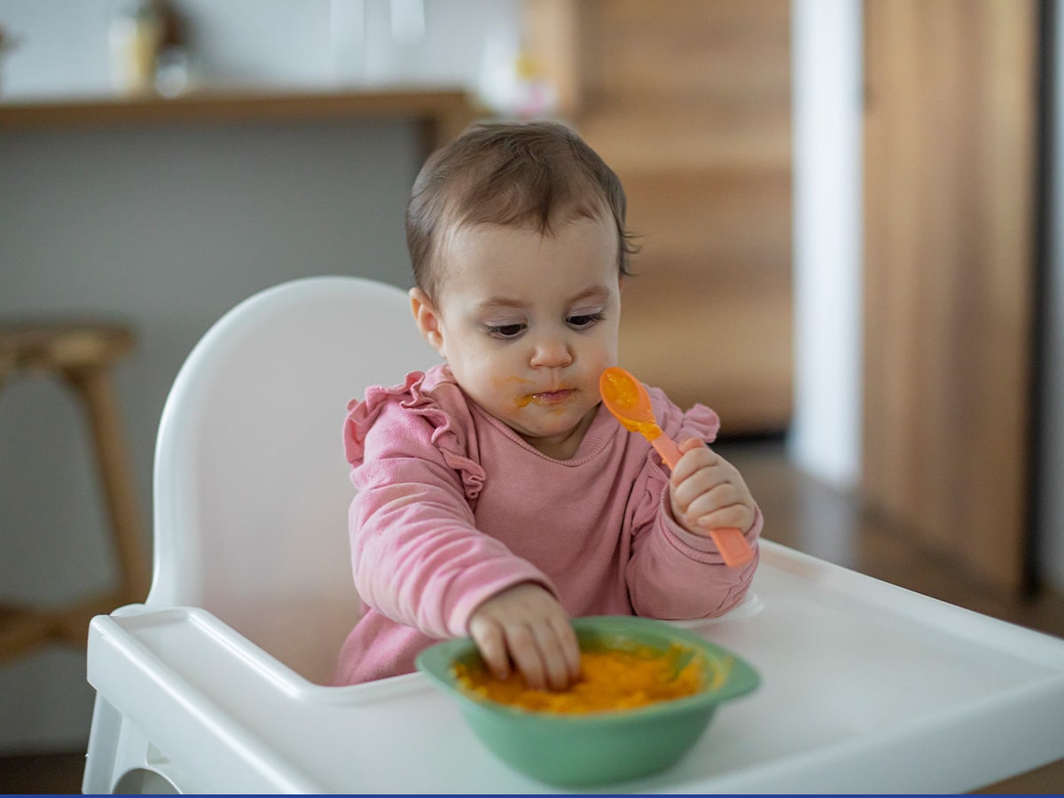 baby in high chair eating baby food puree