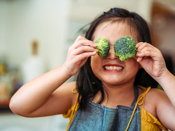 child holding a broccoli floret over each eye