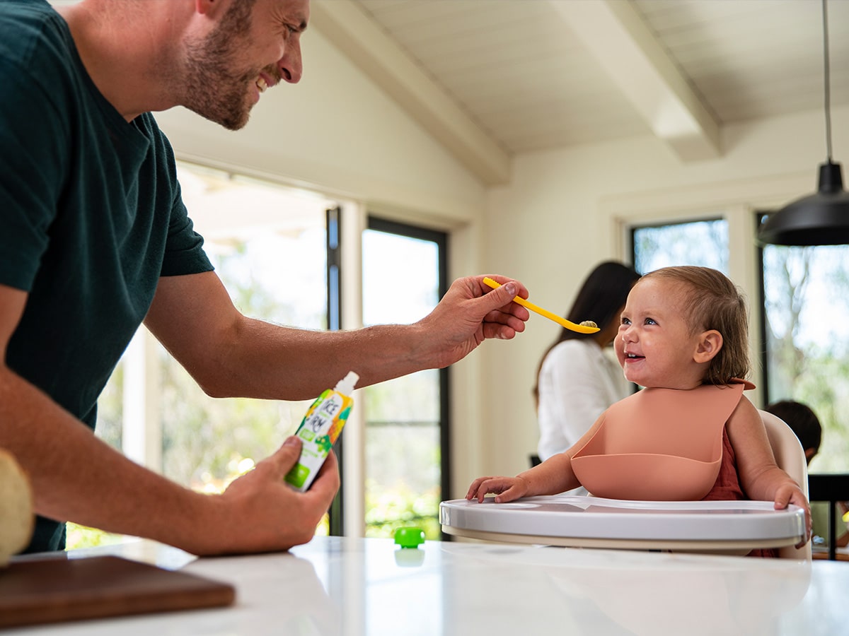 father feeding baby once upon a farm baby food off of a spoon
