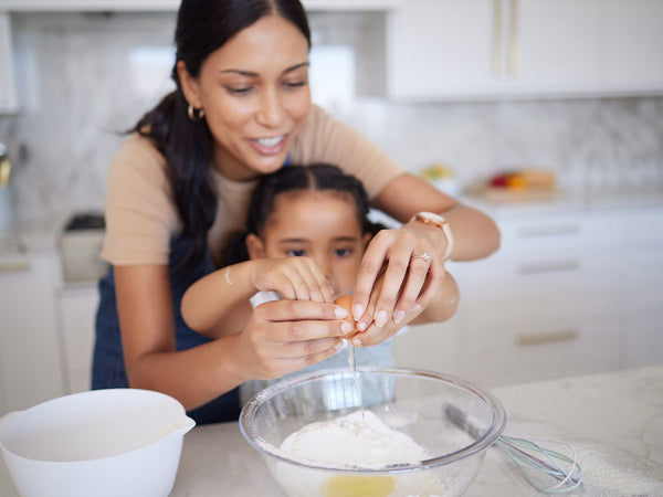 mom helping daughter crack an egg into a mixing bowl