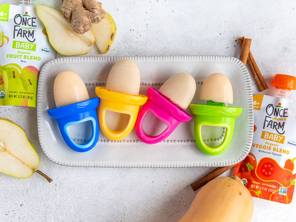 4 baby teething treats, on a tray next to two Once Upon a Farm blends for babies, plus fresh pear, ginger, a butternut squash, and cinnamon sticks