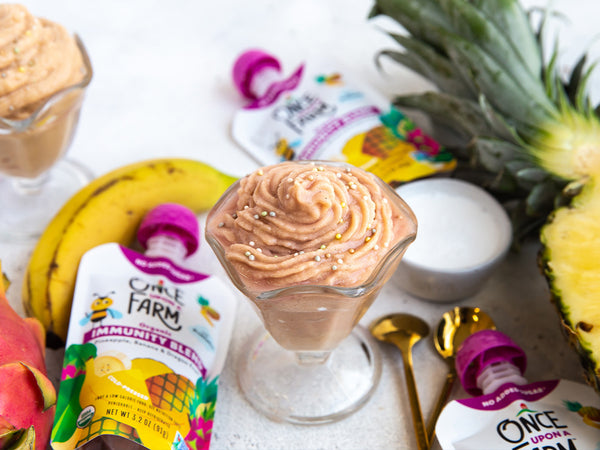 pineapple whip dessert, surrounded by Once Upon a Farm Pineapple, Banana and Dragonfruit Immunity Blend pouches and fresh fruit