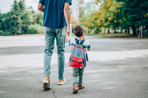 father and son, who's wearing a backpack,  holding hands as they approach school