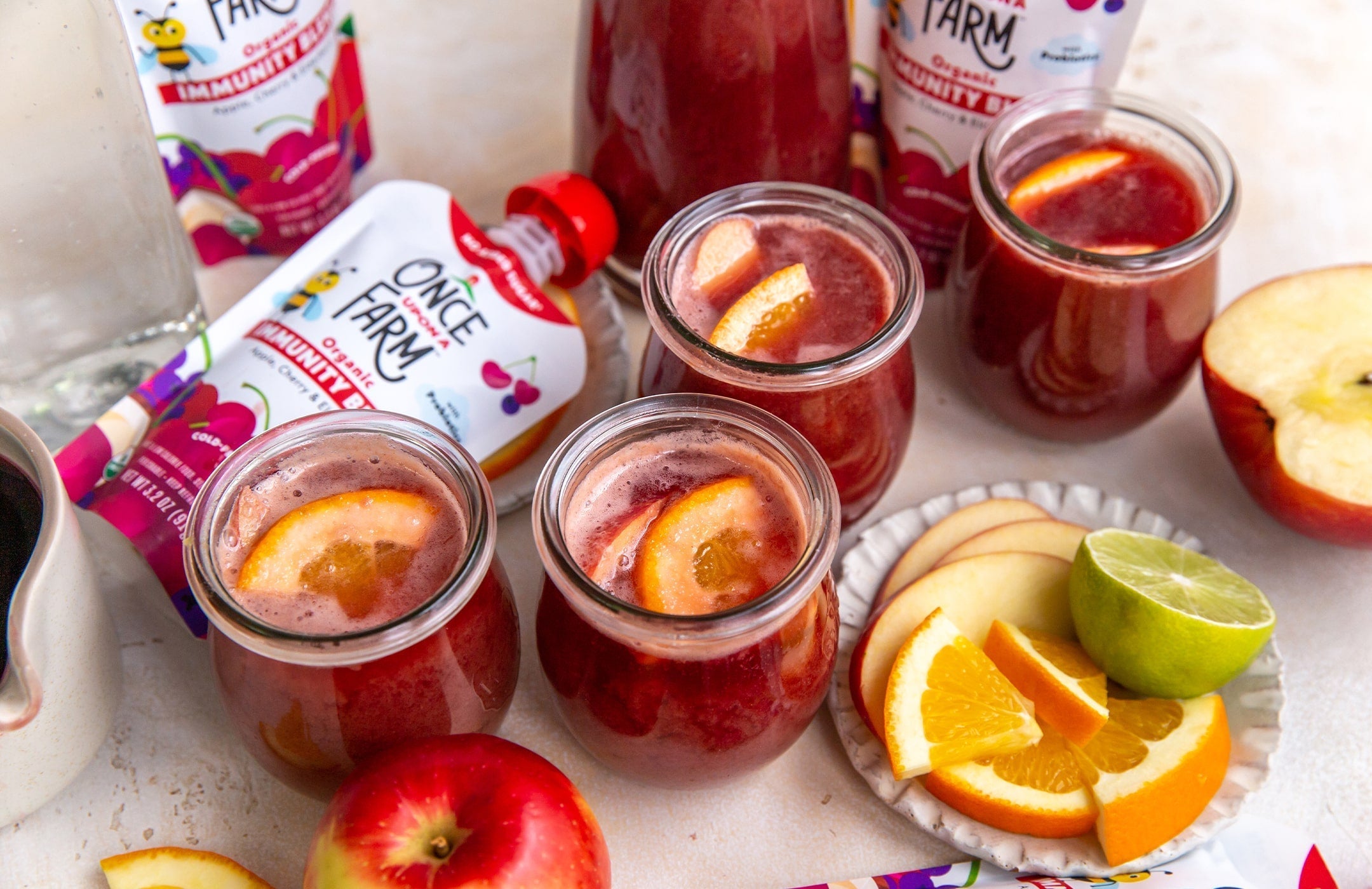 4 fruity mocktails in glasses, next to Once Upon a Farm Apple, Cherry & Elderberry Immunity Blend pouches