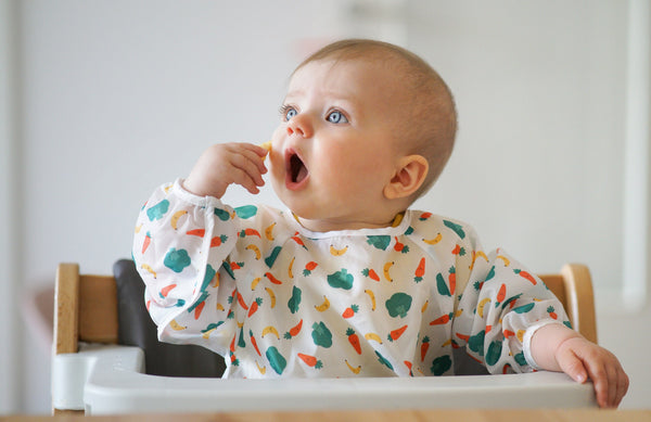 baby holding hand up to mouth while sitting in high chair