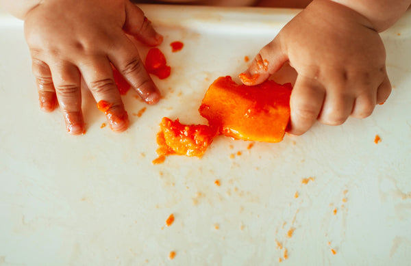 baby hands and a piece of fruit on a high chair tray