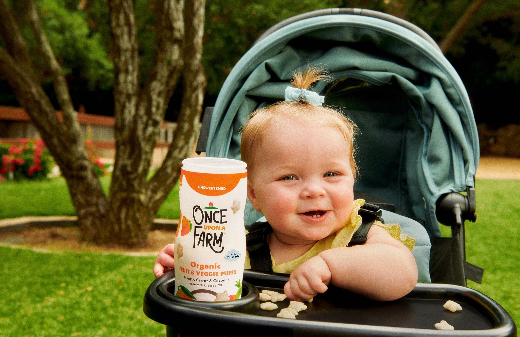 baby in a stroller with a container of Once Upon a Farm Fruit & Veggie Puffs