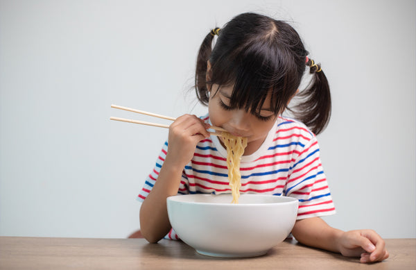 child eating a bowl of noodles with chopsticks