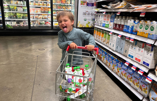 child pushing small grocery cart filled with Once Upon a Farm Dairy-Free Smoothie snack pouches in a grocery store