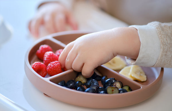 close up of child's hands reaching for berries on a plate of fruit