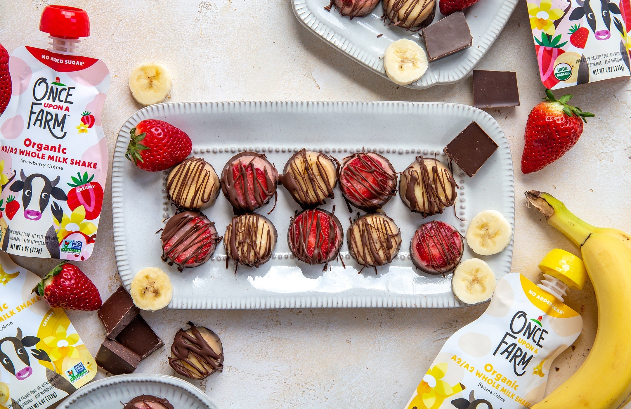 frozen chocolate-covered milkshake bites on a tray, surrounded by Once Upon a Farm pouches, fruit, and chocolate