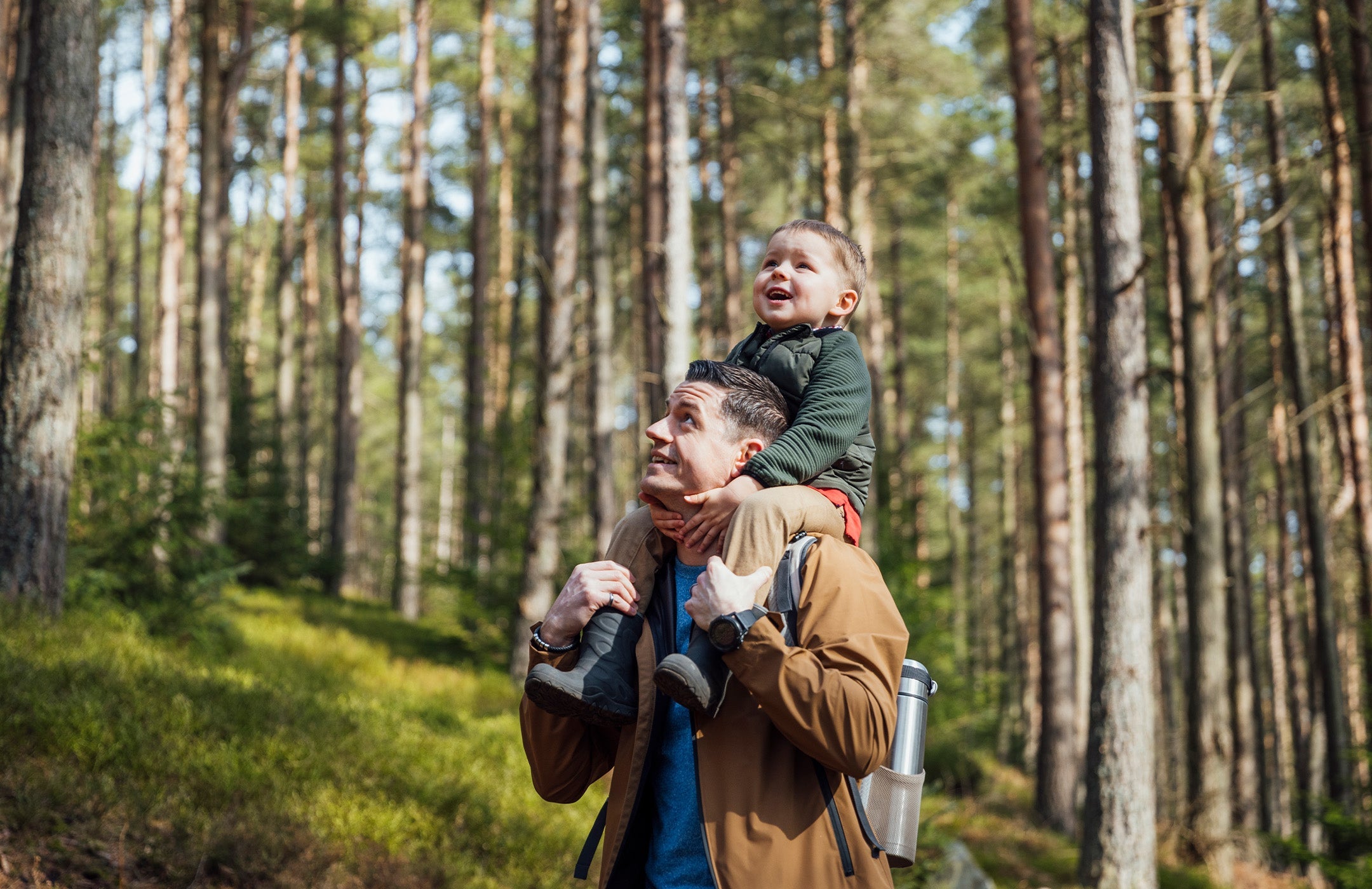dad hiking in the woods with young child on his back