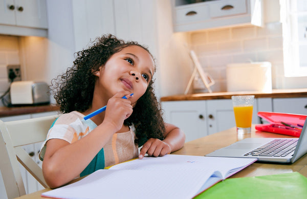 young girl sitting at a kitchen table with a pencil and paper