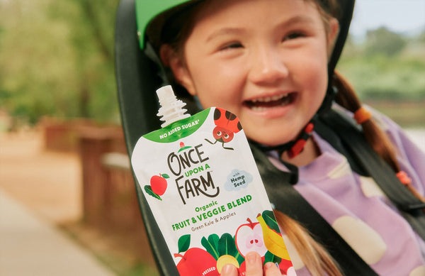 happy young girl on the back of a bicycle, holding a once upon a farm pouch