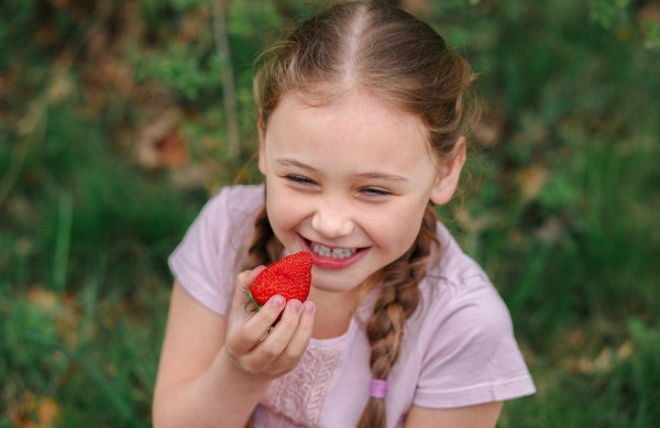 girl smiling while holding a strawberry up to her mouth