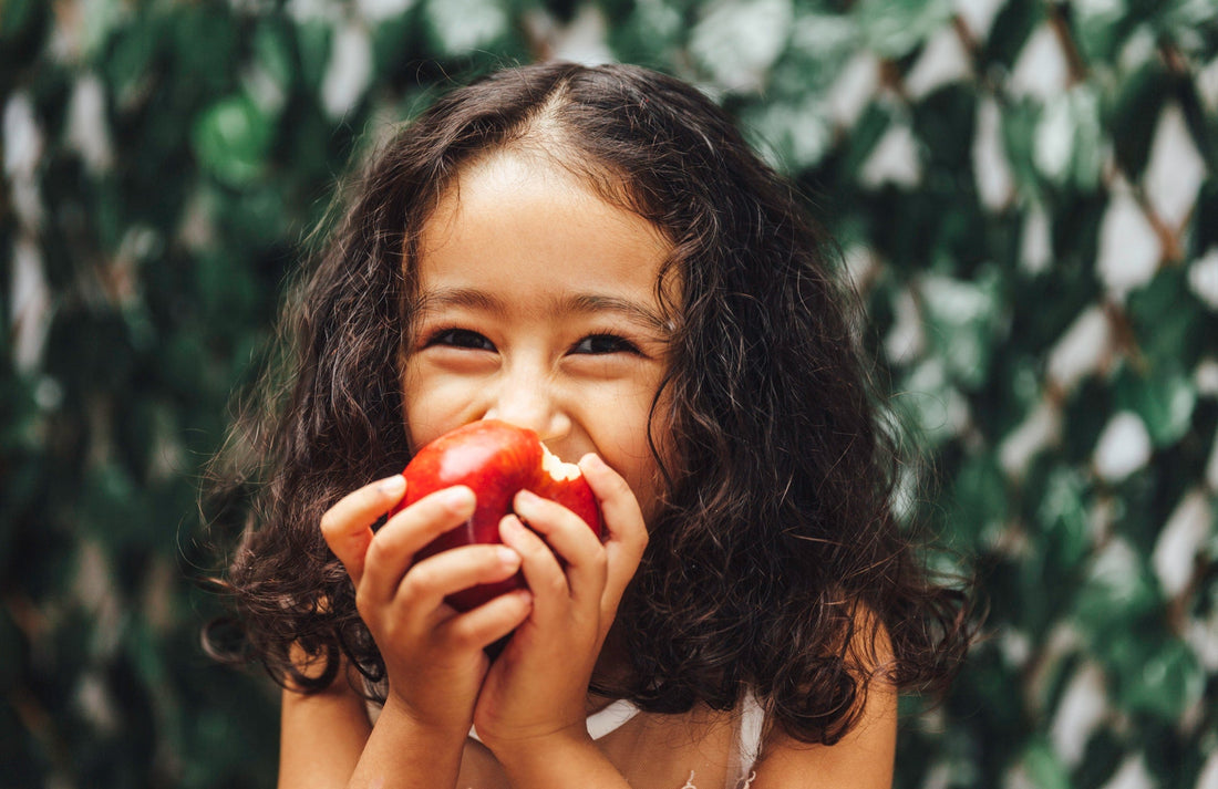 close up of a girl with curly hair biting into an apple