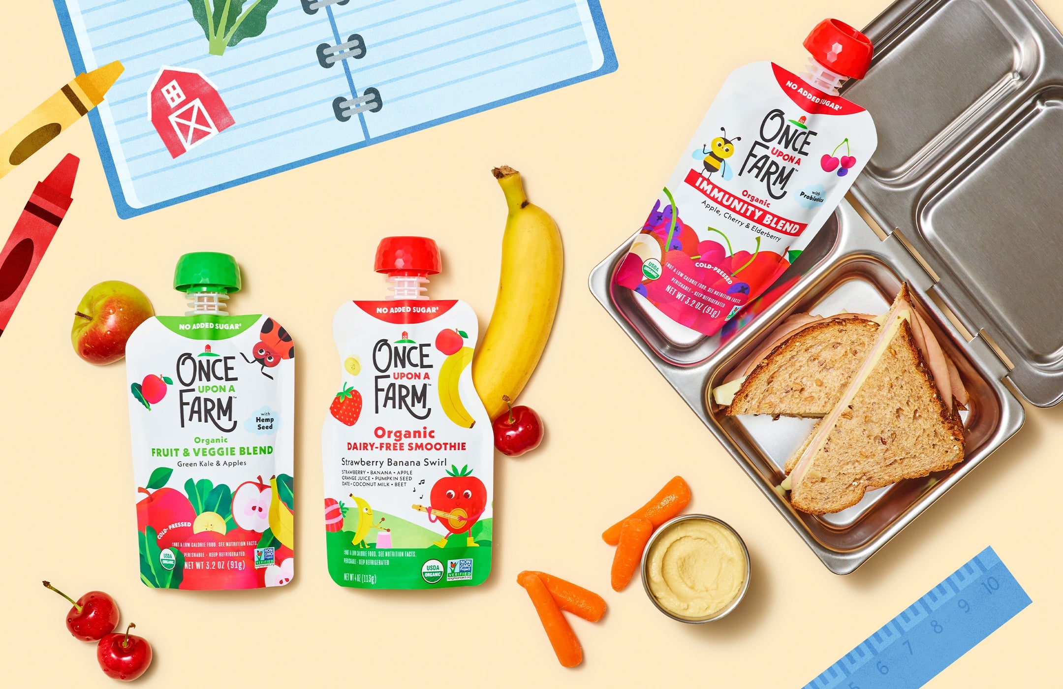 metal lunchbox with a sandwich and Once Upon a Farm pouch inside. Next to it are fresh fruits and veggies and two more Once Upon a Farm pouches