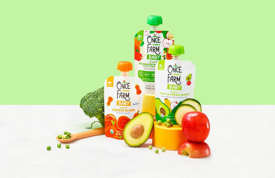 3 Once Upon a Farm baby food pouches on a green background, next to fresh fruits and veggies