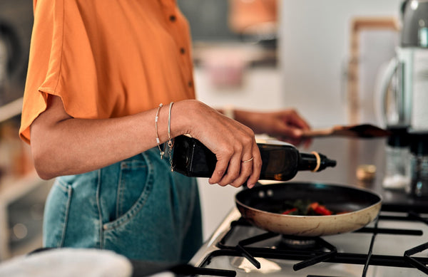 close up of a woman pouring oil into a pan on the stove