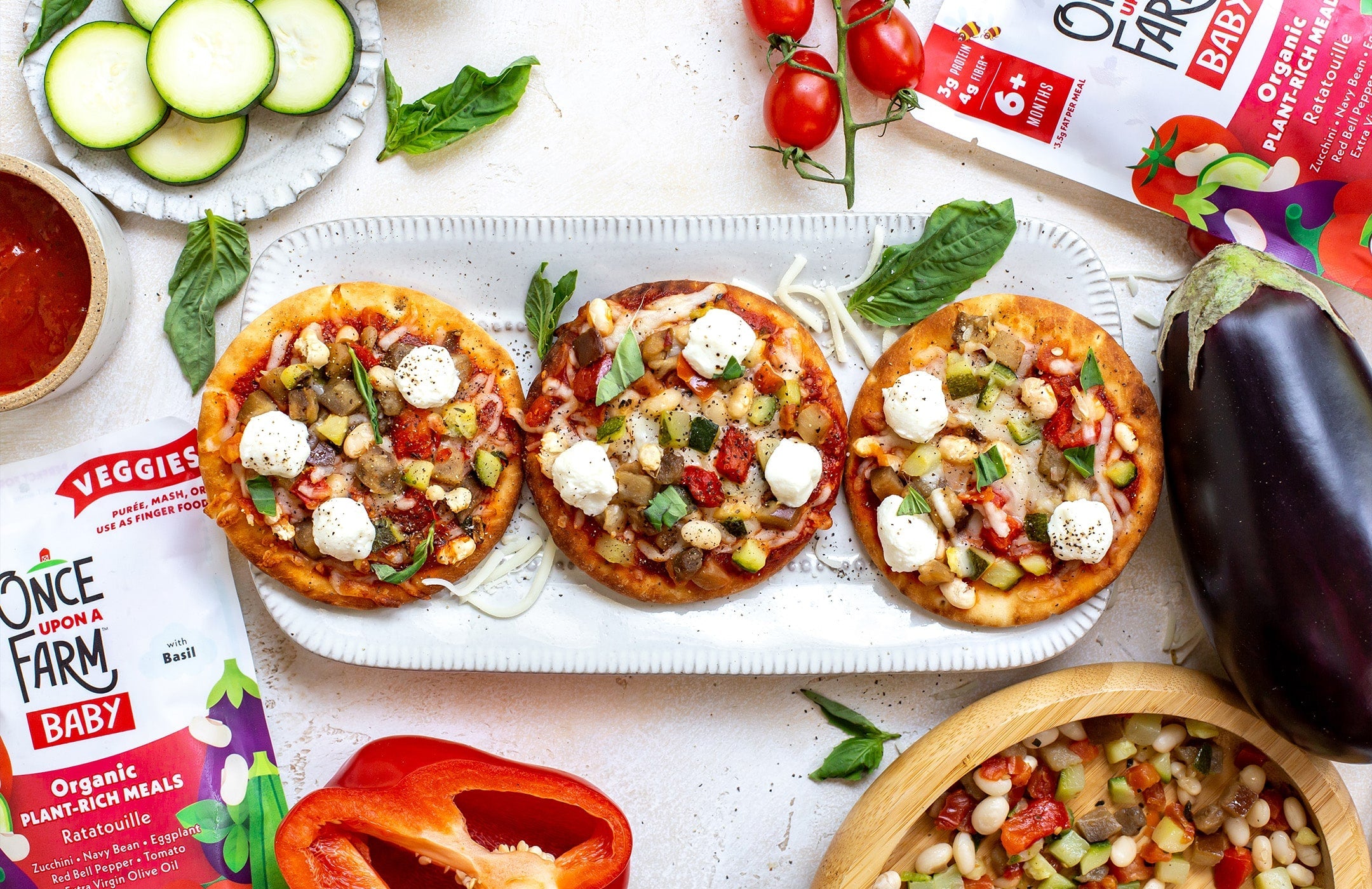 mini pizzas on a plate, surrounded by Once Upon a Farm Ratatouille meals and fresh produce