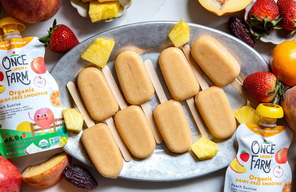 peach sorbet pops on a tray, next to fresh fruit and Once Upon a Farm pouches