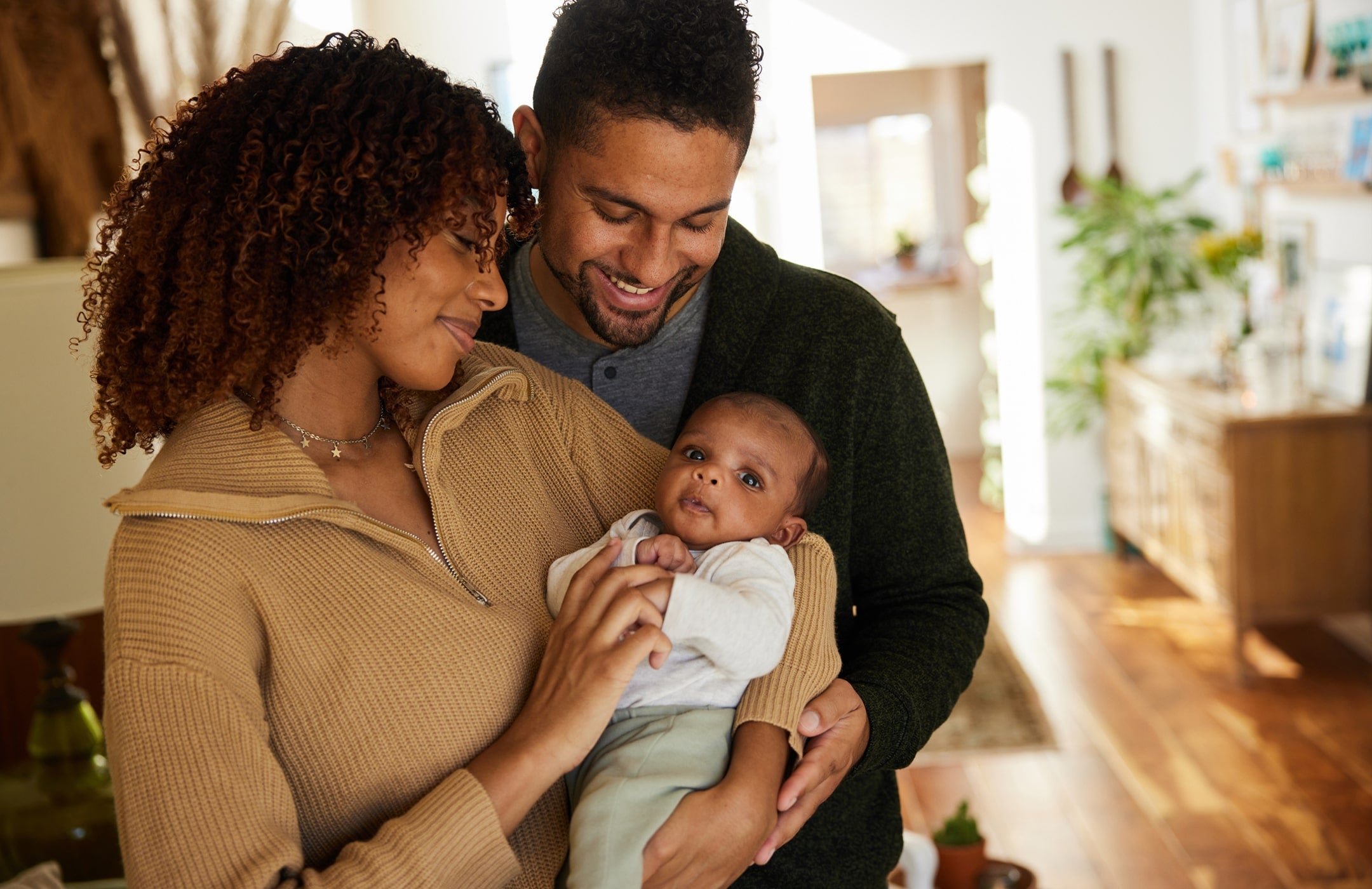 mom holding a newborn baby, while dad wraps his arms around the both of them