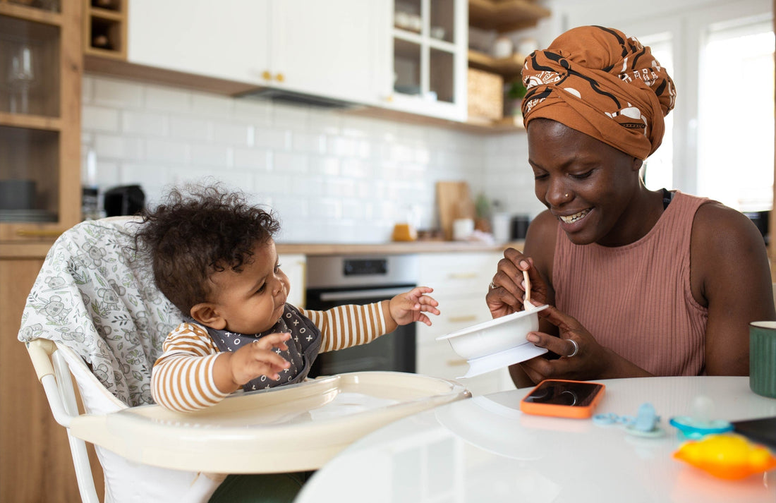 baby reaching for food that mom is holding, while he's sitting in a high chair