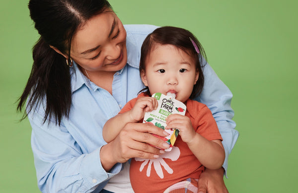 Mom helping toddler eat from a Once Upon a Farm pouch