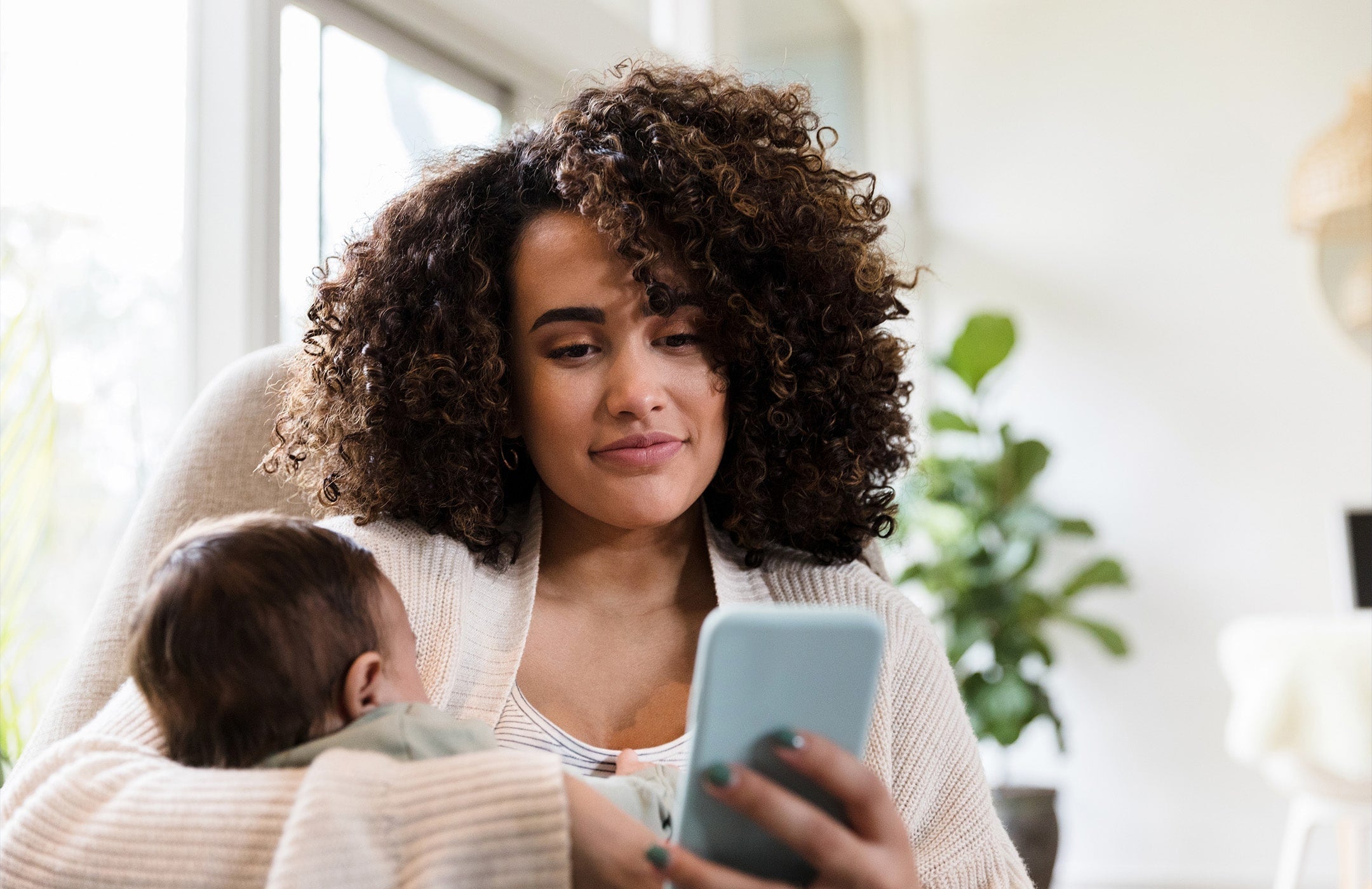 mom looking at her cell phone while holding her baby
