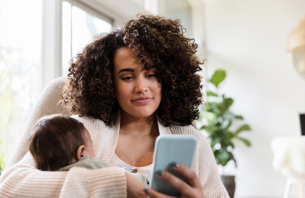 mom looking at her cell phone while holding her baby