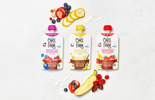 3 flavors of Once Upon a Farm Coconut Milk Yogurt Alternative pouches on a plain background with fresh-cut fruits around them
