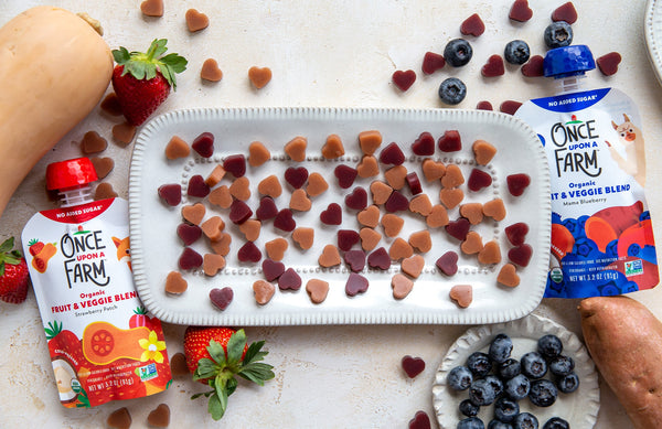 heart-shaped gummies on a tray, surrounded by fresh fruit and veggies and Once Upon a Farm pouches
