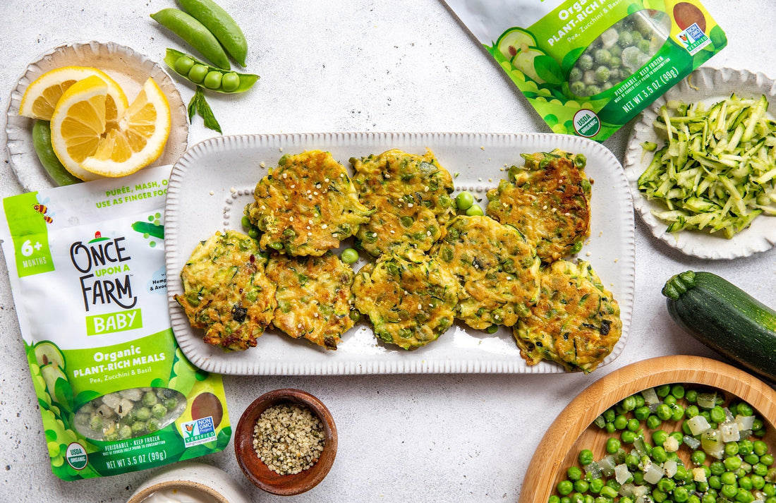 pea and zucchini fritters on a serving plate, surrounded by fresh veggies and Once Upon a Farm meal packages