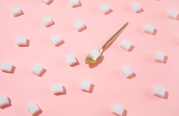assortment of evenly spaced sugar cubes on a pink background. one sugar cube is on a metal spoon