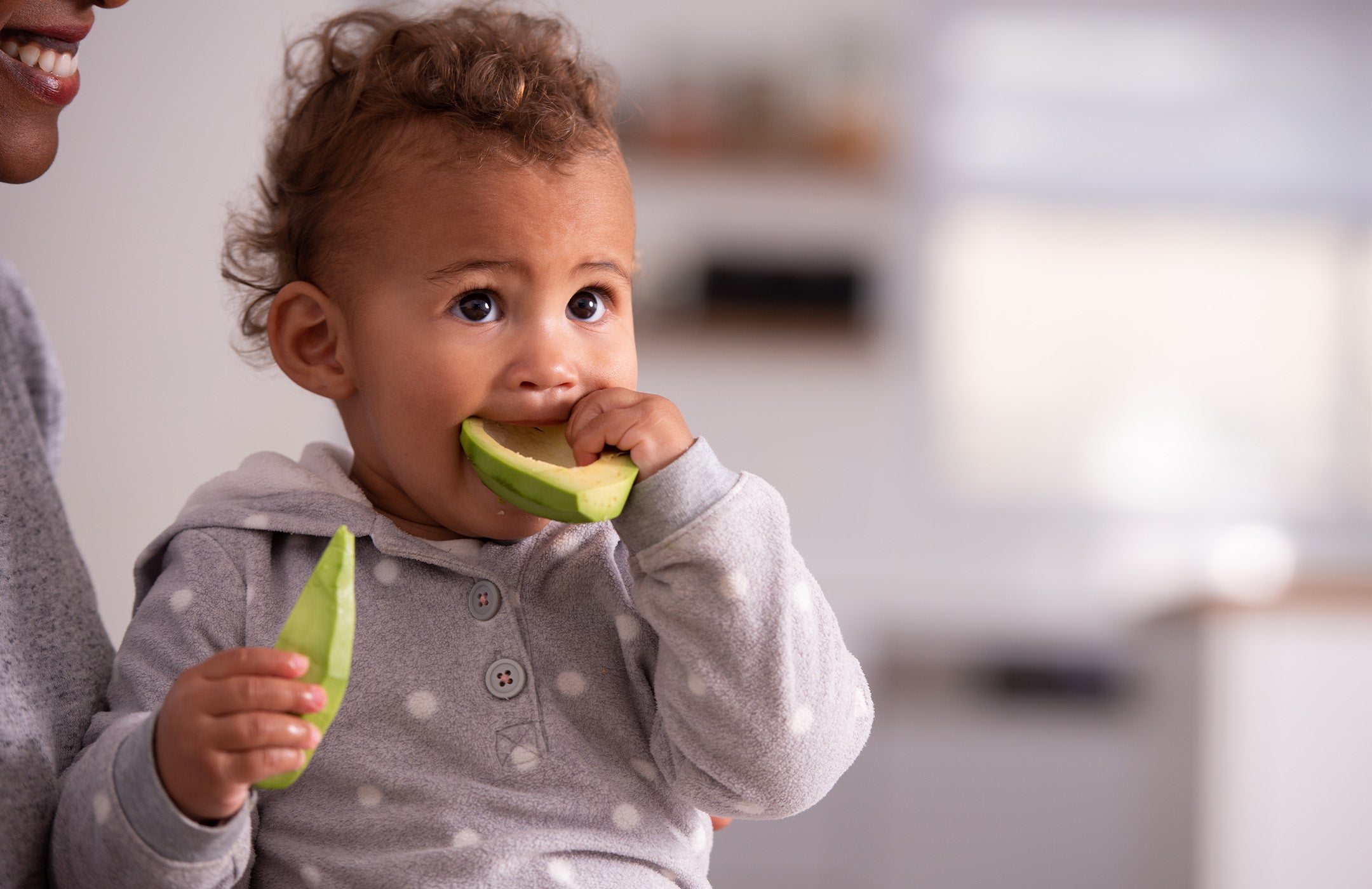 toddler being held by mother and eating an avocado half