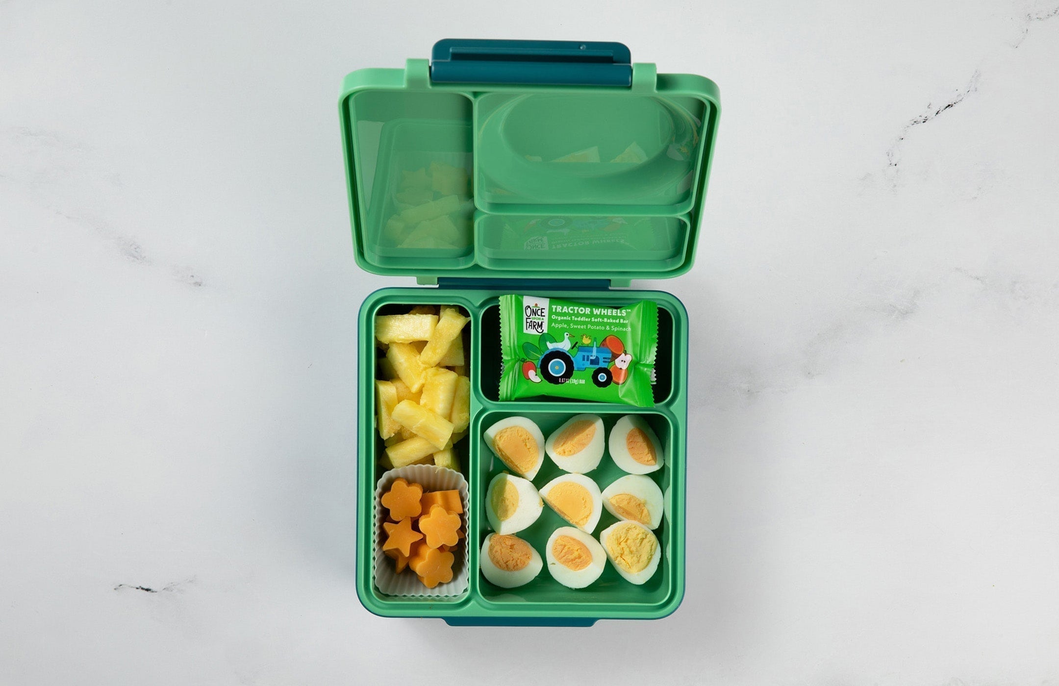 bento box-style lunchbox for a toddler, filled with pineapple chunks, cheese cubes, hard-boiled eggs, and a Once Upon a Farm Tractor Wheel bar