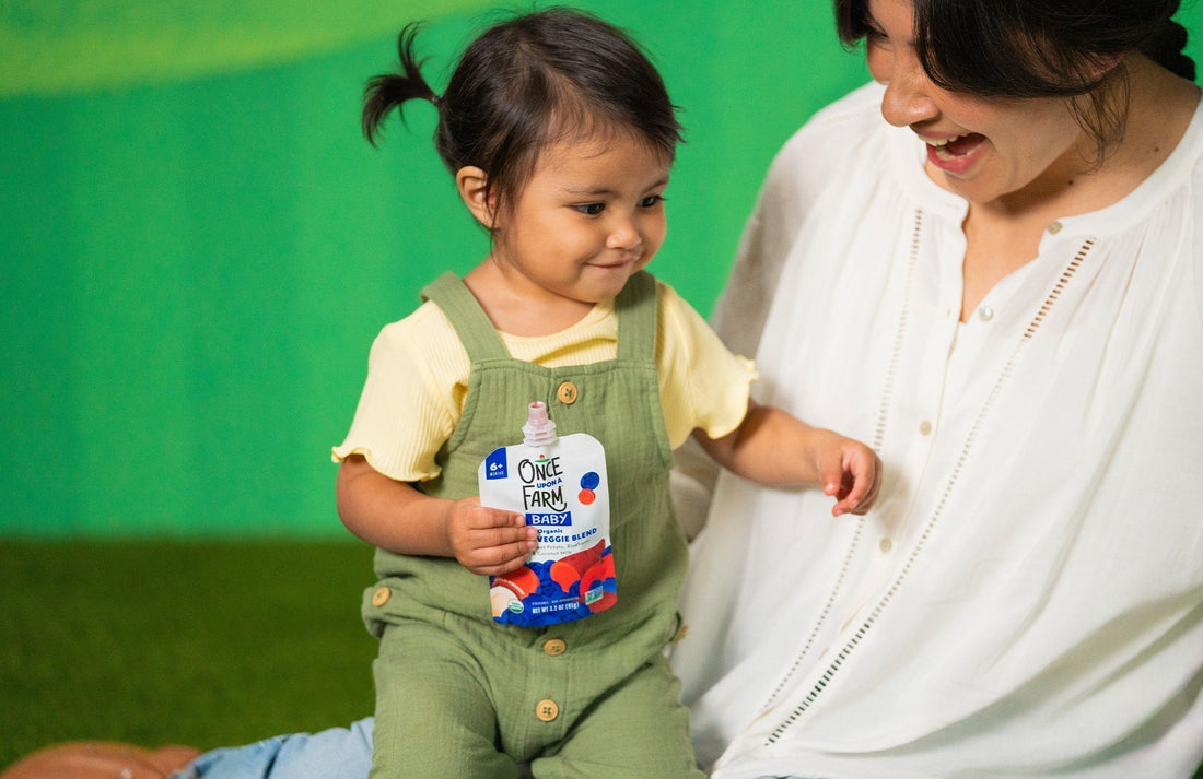 toddler with a Once Upon a Farm baby food pouch on mom's lap