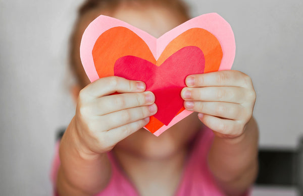 young child holding a homemade valentine's day heart craft