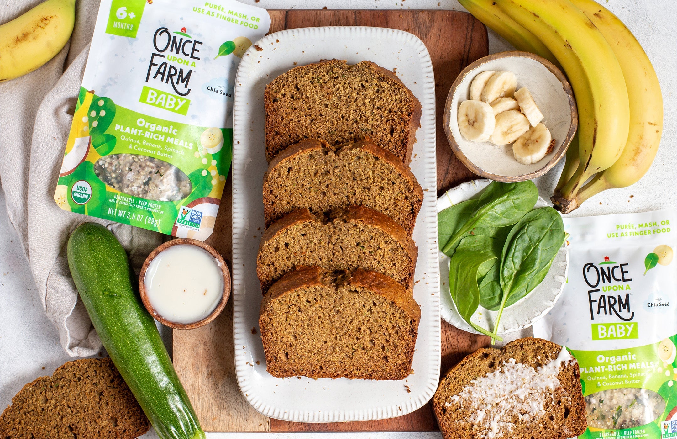 a loaf of sliced banana zucchini bread on a tray, surrounded by fresh ingredients and a Once Upon a Farm Plant-Rich Meal