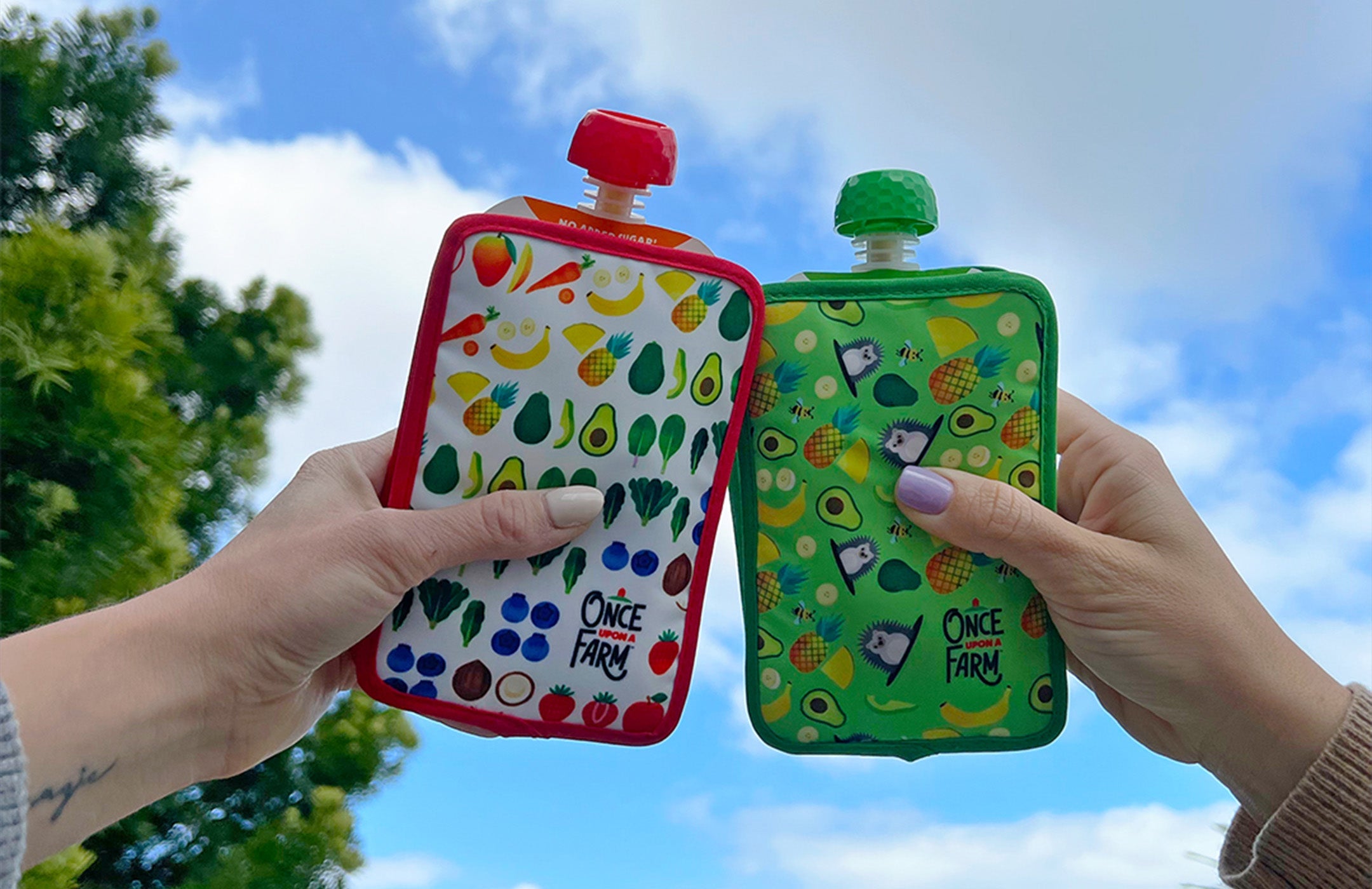 Two hands holding Once Upon a Farm pouches in Pouch Coolers up in the air