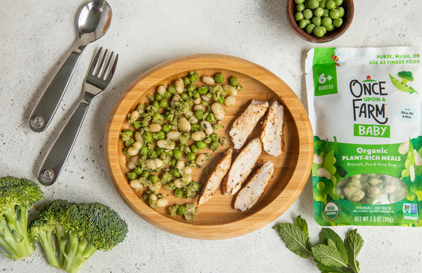 Once Upon a Farm Pea, Zucchini & Basil meal on a plate next to some grilled and sliced chicken, next to fresh broccoli, peas, mint, and the Once Upon a Farm packaging