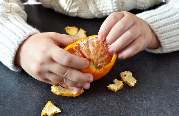 child's hands peeling a mandarin orange 
