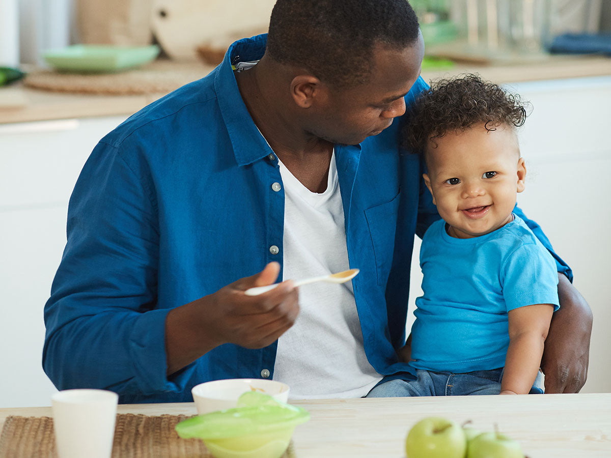 Dad spoon-feeding his son baby food. 