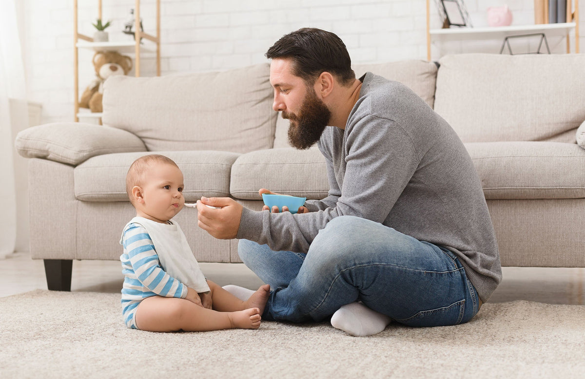 Dad spoon-feeding his son baby food. 